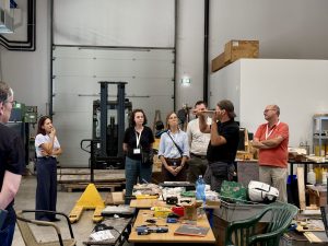 A tour group of people stand and listen to a guide in the Composites Laboratory at InnoRenew CoE. The guide shows a wooden samples.